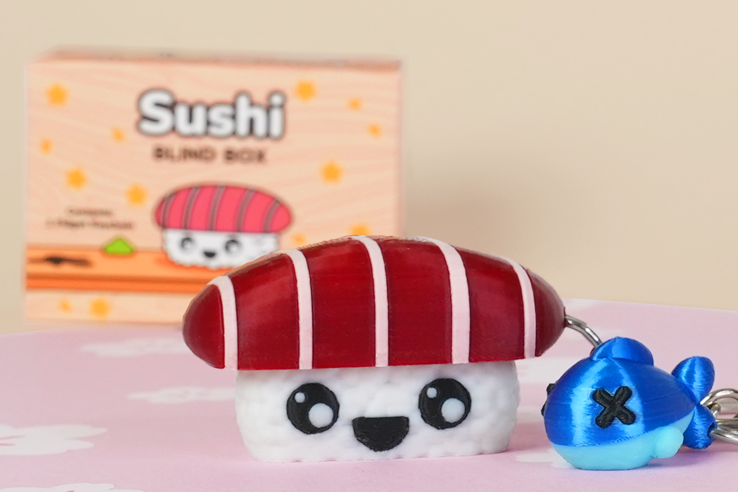 Sushi-themed keychain with a small blue fish charm on a pink surface, with a 'Sushi' blind box in the background.
